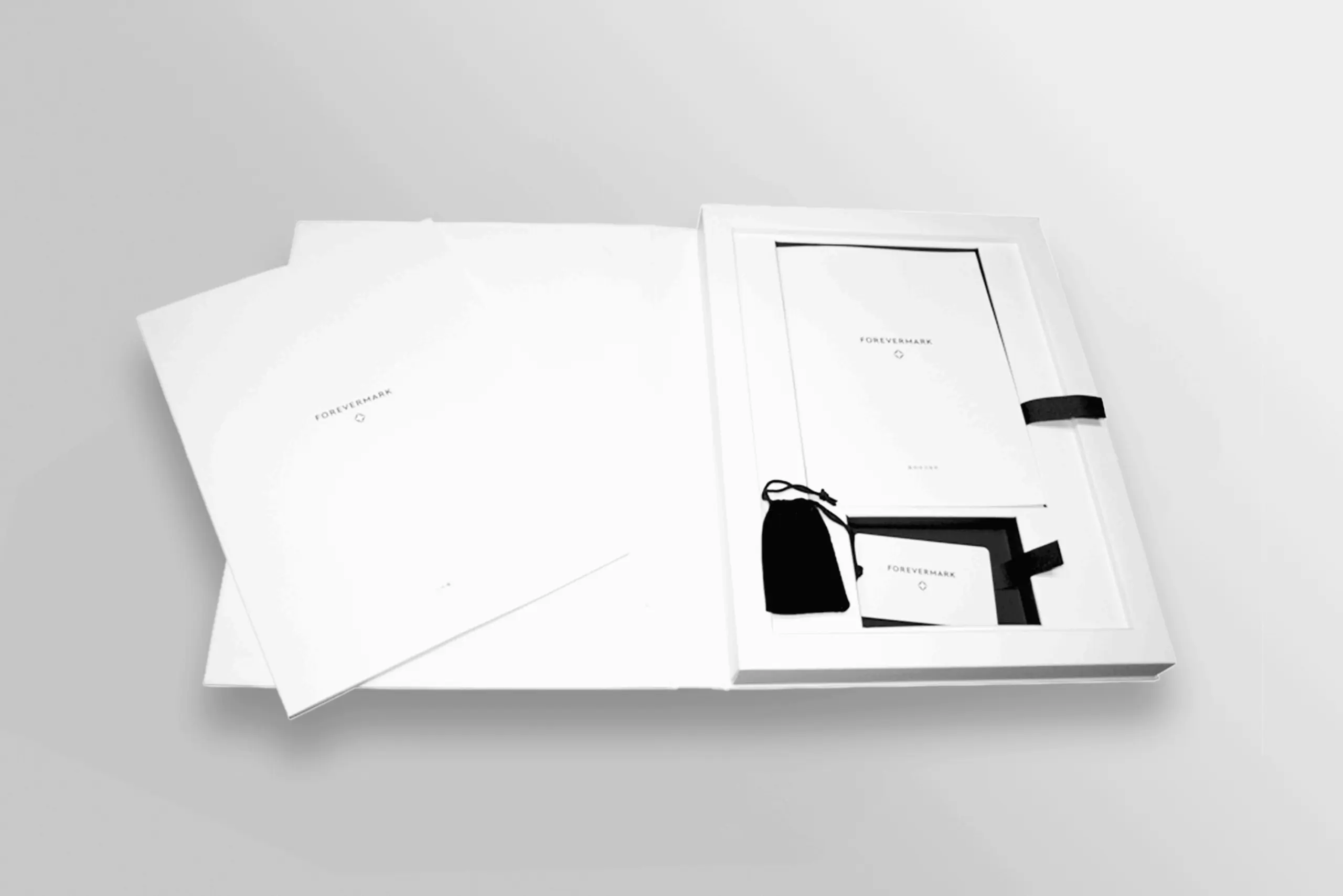 Forevermark packaging including elegant stationery set featuring minimalistic white design and black ribbon accents.