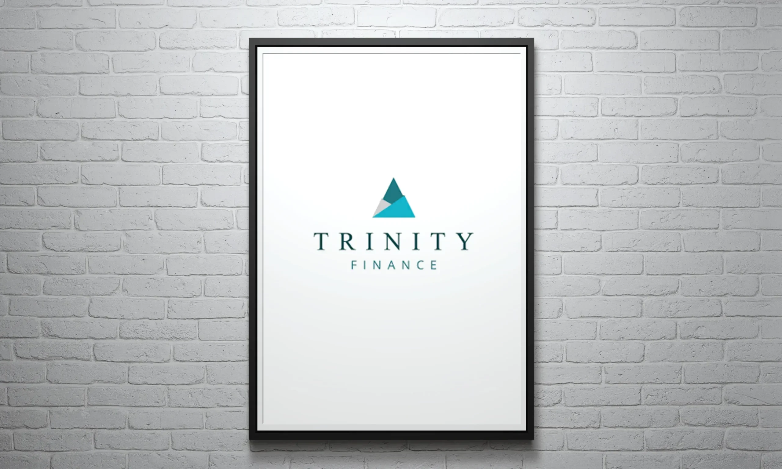 WarmRed Creative presents a framed Trinity Finance poster featuring a sleek logo design with a blue triangular icon on a minimalist white brick wall background.